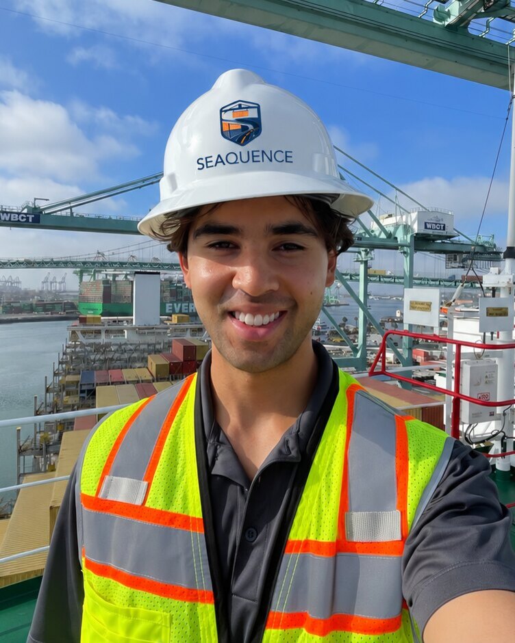 Blake Jones in a Seaquence hard hat on a vessel at the Port of Los Angeles, with quay cranes behind him.